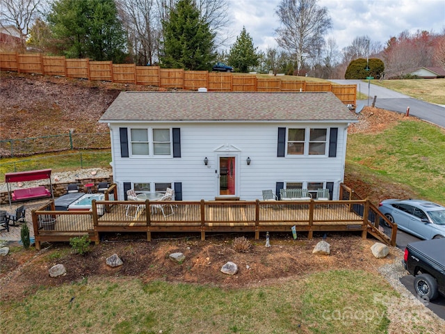 view of front of house featuring a front lawn, roof with shingles, fence, and a wooden deck