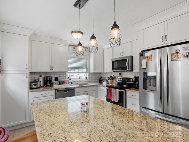 kitchen with a sink, white cabinets, appliances with stainless steel finishes, decorative backsplash, and pendant lighting