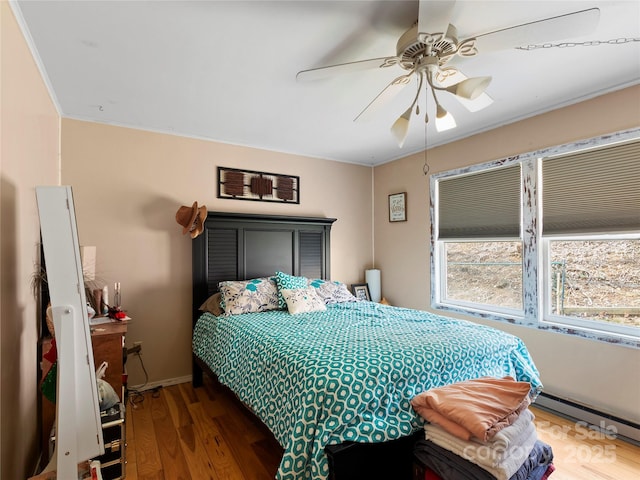 bedroom with baseboards, ceiling fan, wood finished floors, baseboard heating, and crown molding