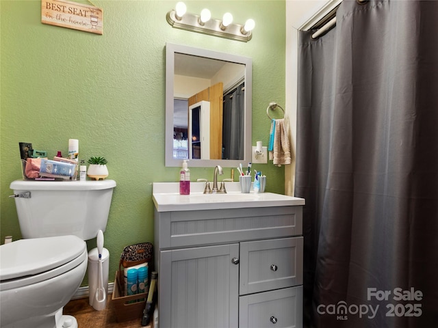 full bath with a textured wall, vanity, and toilet