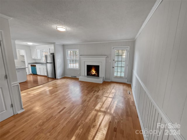 unfurnished living room with light hardwood / wood-style flooring, a textured ceiling, a fireplace, and plenty of natural light