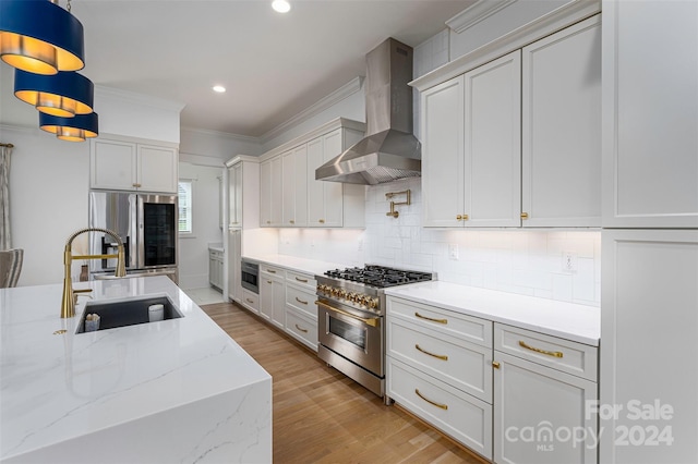 kitchen with stainless steel appliances, sink, wall chimney range hood, pendant lighting, and white cabinets