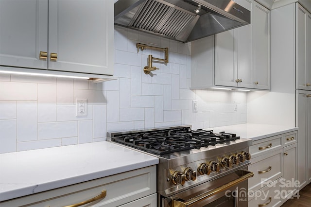 kitchen with high end range, gray cabinetry, light stone counters, and wall chimney exhaust hood