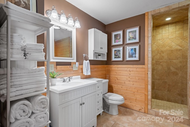 bathroom featuring toilet, vanity, tile patterned floors, wooden walls, and a tile shower