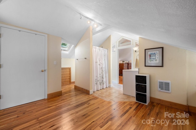 additional living space featuring light wood-type flooring, vaulted ceiling with skylight, and a textured ceiling