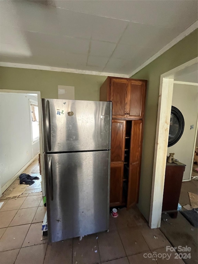 kitchen with stainless steel fridge, ornamental molding, and light tile floors