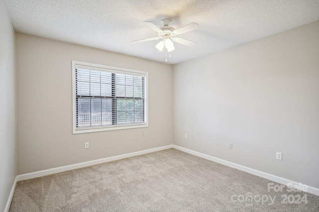 empty room with ceiling fan, light colored carpet, and a textured ceiling