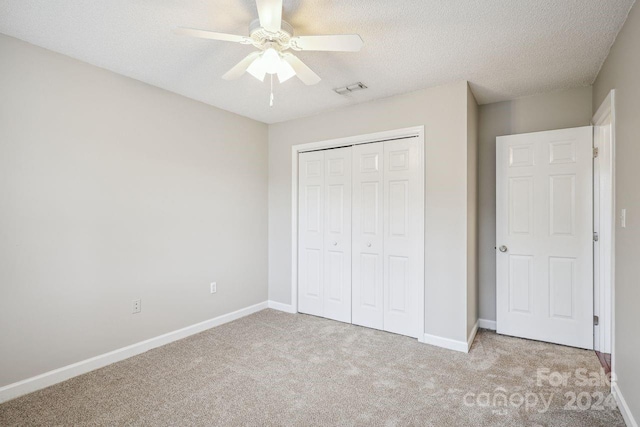 unfurnished bedroom featuring a closet, light carpet, a textured ceiling, and ceiling fan