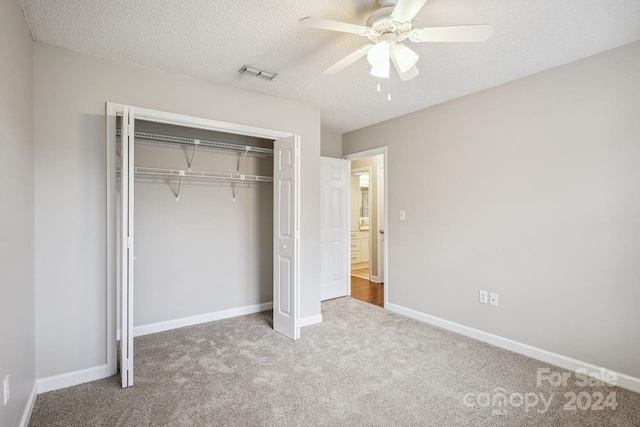 unfurnished bedroom with a closet, a textured ceiling, light colored carpet, and ceiling fan