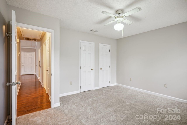 unfurnished bedroom with dark carpet, two closets, ceiling fan, and a textured ceiling