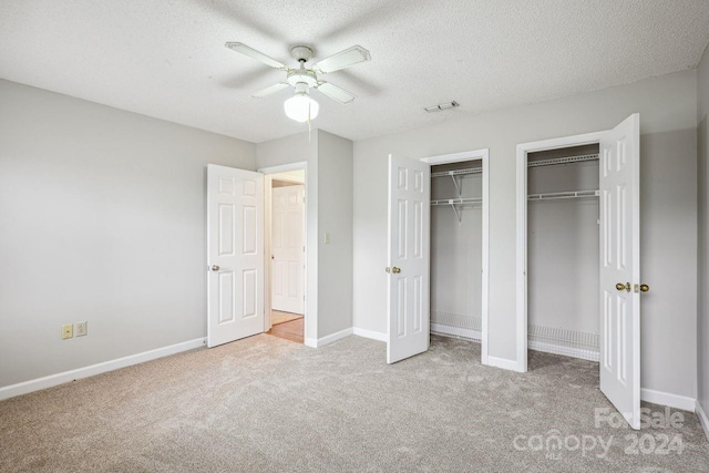 unfurnished bedroom with a textured ceiling, light colored carpet, ceiling fan, and multiple closets