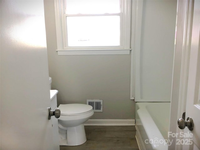 bathroom with hardwood / wood-style flooring, a bathing tub, and toilet