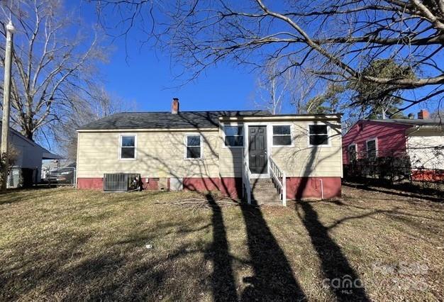 rear view of property featuring central AC unit and a lawn