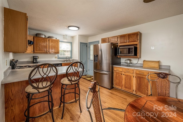 kitchen with appliances with stainless steel finishes, a textured ceiling, a kitchen bar, and light wood-type flooring