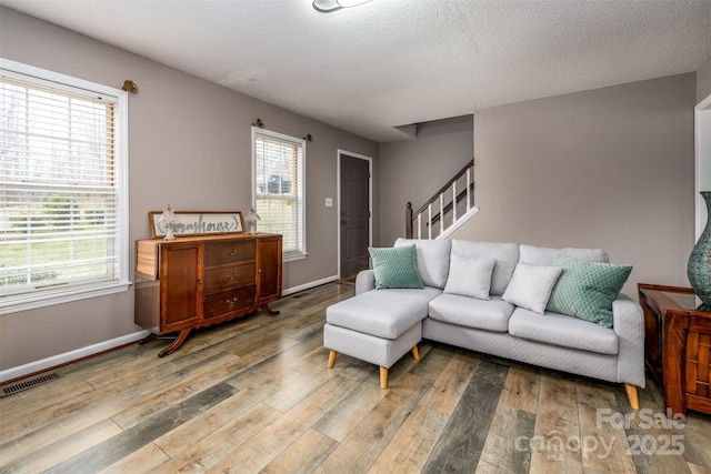 living area featuring light wood finished floors, visible vents, stairway, and baseboards