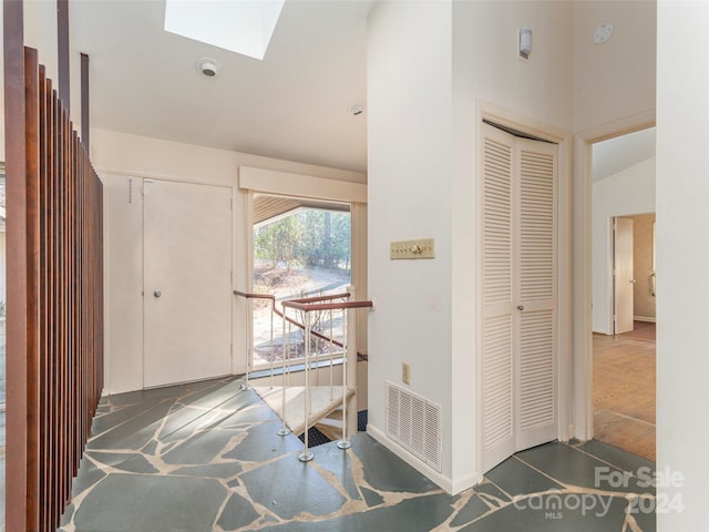 foyer entrance featuring lofted ceiling with skylight and dark tile floors