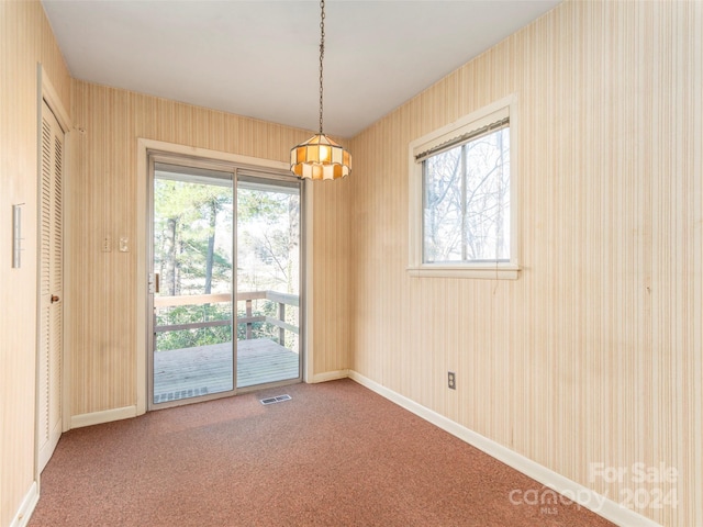 carpeted spare room featuring a notable chandelier and a wealth of natural light