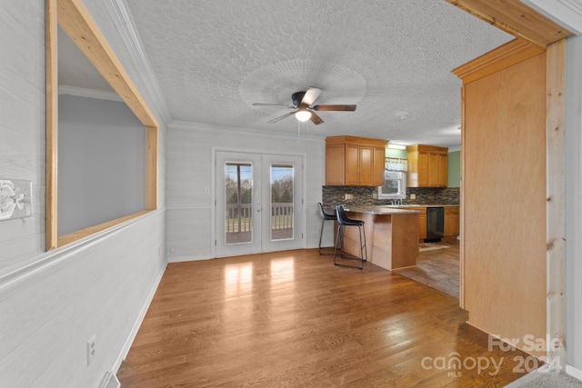 kitchen with light hardwood / wood-style floors, ceiling fan, tasteful backsplash, ornamental molding, and a breakfast bar area