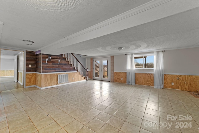 unfurnished living room featuring french doors, wood walls, a textured ceiling, and light tile floors