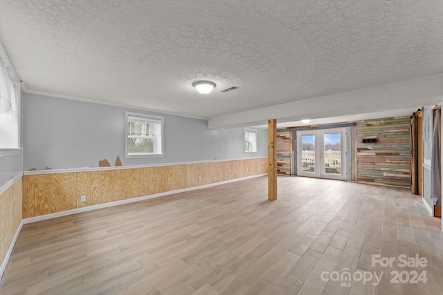 unfurnished room with a textured ceiling, light hardwood / wood-style flooring, french doors, and a wealth of natural light