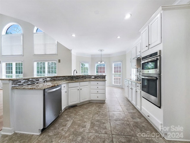 kitchen featuring appliances with stainless steel finishes, dark stone countertops, white cabinets, hanging light fixtures, and kitchen peninsula