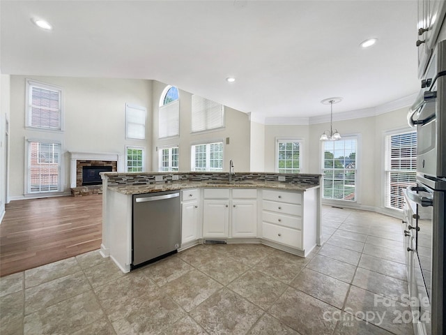 kitchen featuring sink, white cabinetry, hanging light fixtures, a stone fireplace, and stainless steel dishwasher