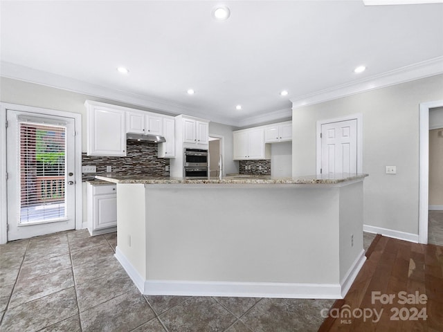 kitchen featuring a kitchen island with sink, double oven, white cabinetry, and light stone countertops