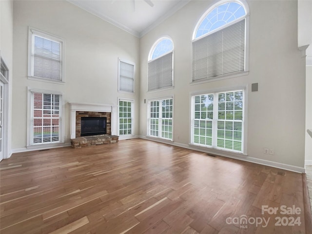 unfurnished living room with ornamental molding, a stone fireplace, a towering ceiling, and hardwood / wood-style floors