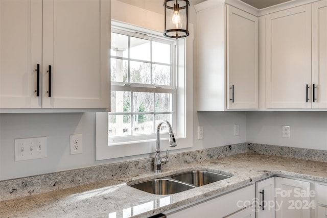 kitchen with light stone counters, white cabinetry, and sink