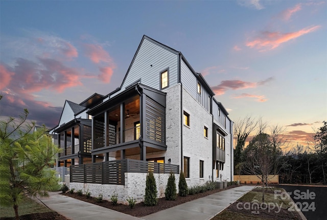 property exterior at dusk featuring a balcony and cooling unit