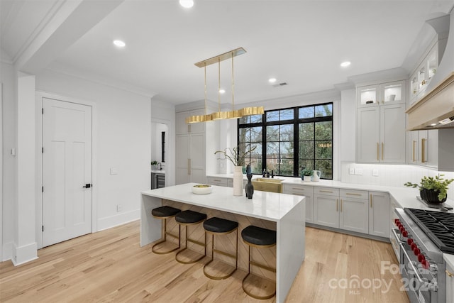 kitchen featuring decorative light fixtures, range with two ovens, a kitchen island, custom range hood, and light hardwood / wood-style flooring