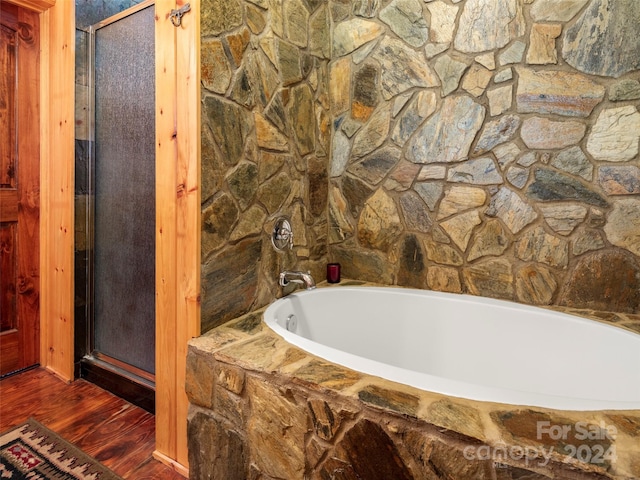 bathroom featuring wood-type flooring and a relaxing tiled tub