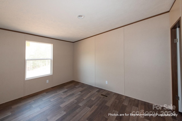 empty room with a textured ceiling, dark wood-type flooring, and ornamental molding