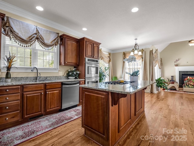 kitchen with sink, decorative light fixtures, a kitchen island, stainless steel appliances, and light hardwood / wood-style floors