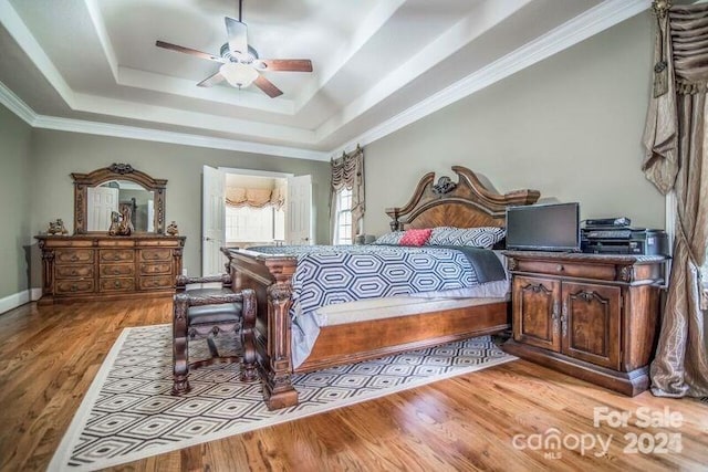 bedroom with ceiling fan, ornamental molding, a tray ceiling, and light hardwood / wood-style floors