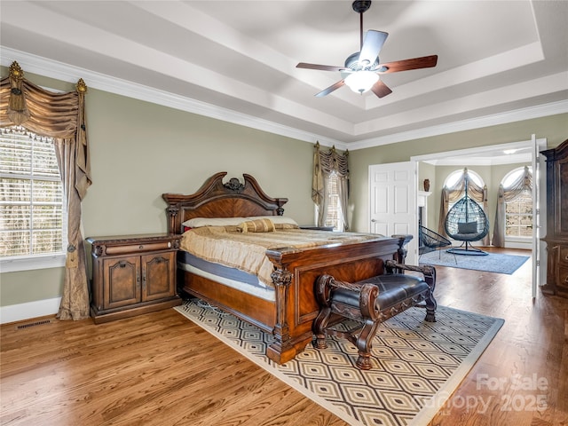 bedroom with ceiling fan, ornamental molding, a tray ceiling, and light hardwood / wood-style floors