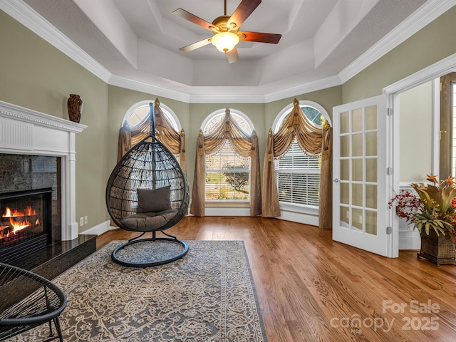 living area featuring crown molding, ceiling fan, a high end fireplace, a raised ceiling, and light wood-type flooring