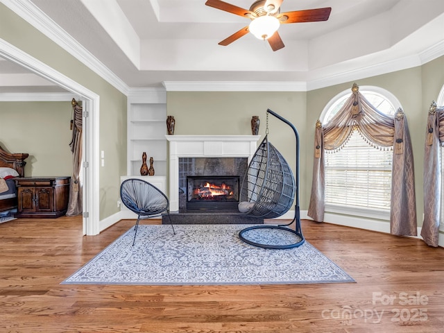 sitting room featuring crown molding, a tray ceiling, built in features, hardwood / wood-style flooring, and a fireplace