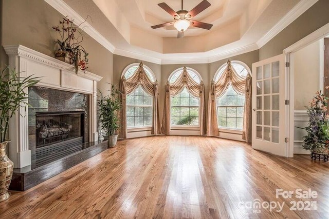 unfurnished living room featuring a fireplace, ornamental molding, ceiling fan, a raised ceiling, and light hardwood / wood-style flooring