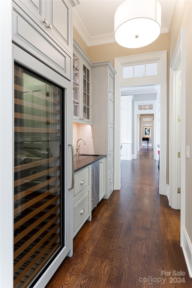 kitchen with dark stone counters, dark hardwood / wood-style flooring, beverage cooler, sink, and crown molding