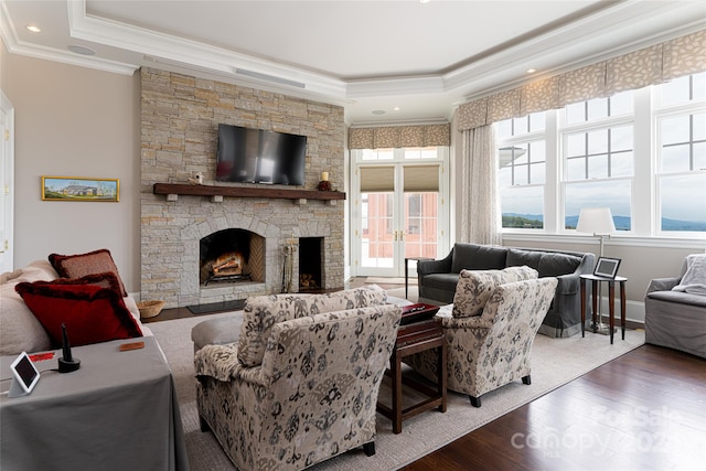 living room featuring a tray ceiling, dark hardwood / wood-style flooring, a stone fireplace, and crown molding