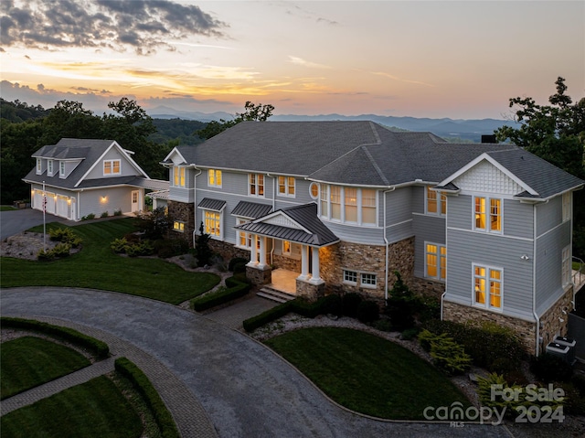 shingle-style home with a front lawn, stone siding, concrete driveway, and a garage