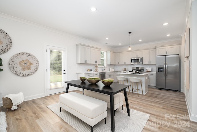 kitchen with appliances with stainless steel finishes, pendant lighting, crown molding, tasteful backsplash, and light hardwood / wood-style flooring