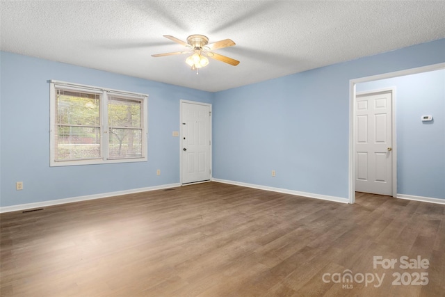 spare room featuring a textured ceiling, visible vents, baseboards, a ceiling fan, and wood finished floors