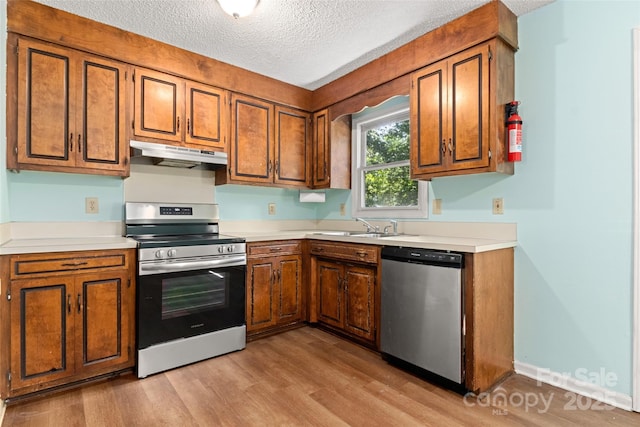 kitchen featuring brown cabinets, under cabinet range hood, stainless steel appliances, and a sink