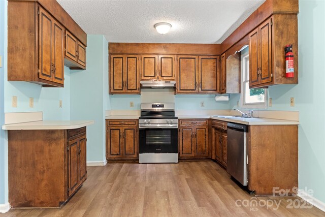 kitchen featuring light wood-style flooring, brown cabinets, light countertops, under cabinet range hood, and appliances with stainless steel finishes