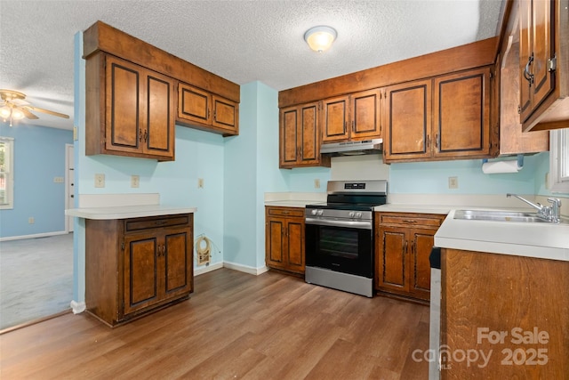kitchen with a sink, a textured ceiling, brown cabinets, stainless steel range with electric cooktop, and under cabinet range hood