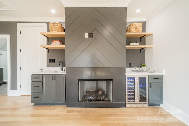 bar with light wood-type flooring, gray cabinetry, wine cooler, and sink