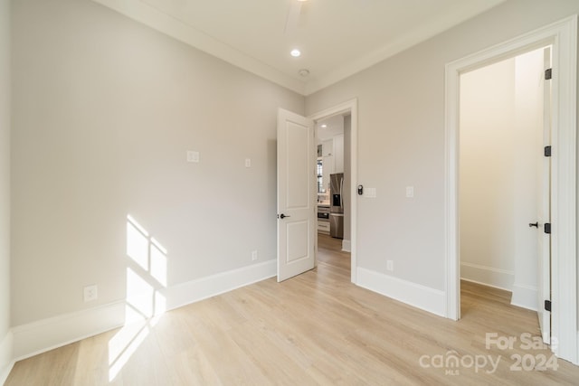 unfurnished bedroom featuring stainless steel refrigerator with ice dispenser, ceiling fan, crown molding, and light wood-type flooring