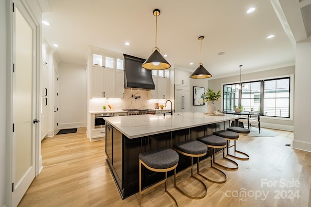 kitchen with premium range hood, a spacious island, decorative light fixtures, light wood-type flooring, and white cabinets